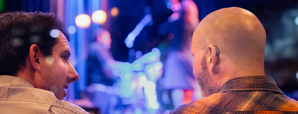 Image of two men talking during a concert and one of them is wearing a hearing aid